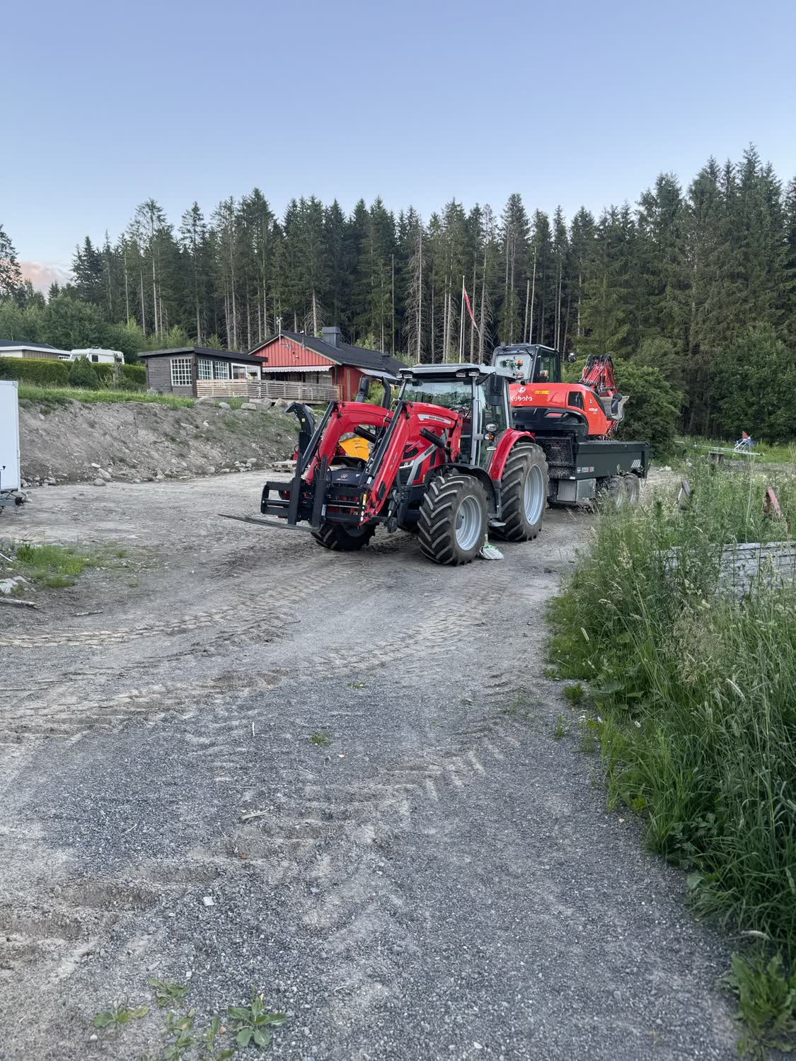 Traktor med boggihenger på grusvei ved gårdstun i Innlandet